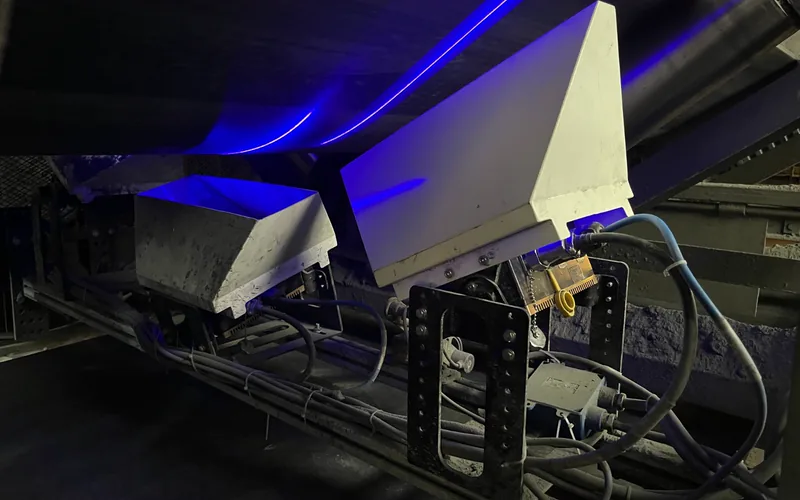 Cabeçote do sistema TDIS instalado sob uma correia transportadora, com o feixe de laser azul atravessando a lona