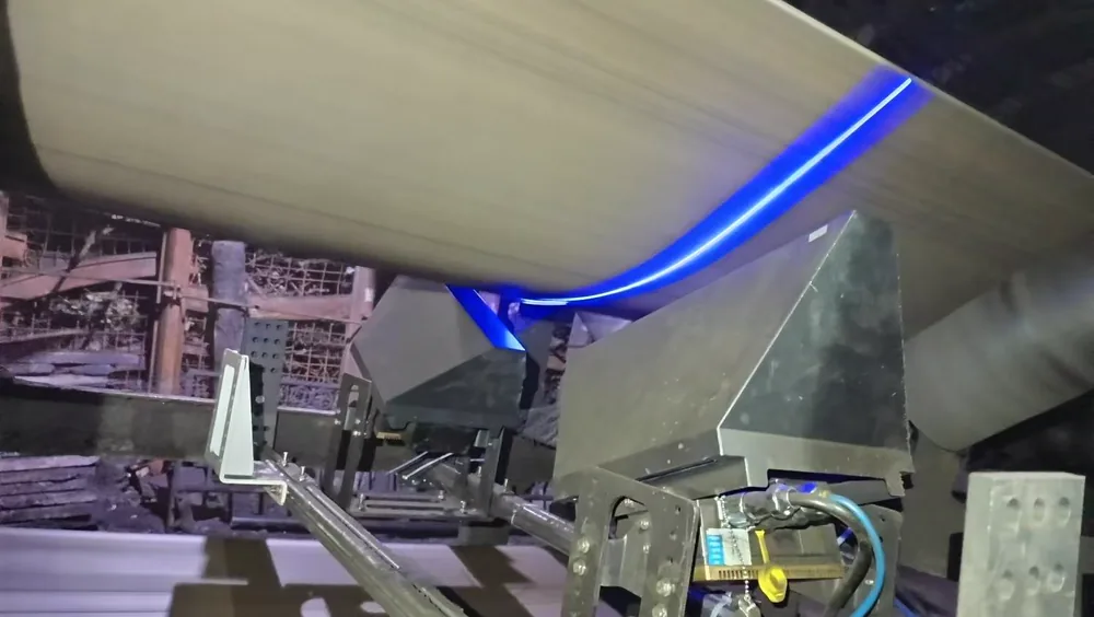 Sistema TDIS da DMC Technology em operação: linha de laser azul varrendo a superfície de uma correia transportadora em galeria de transporte